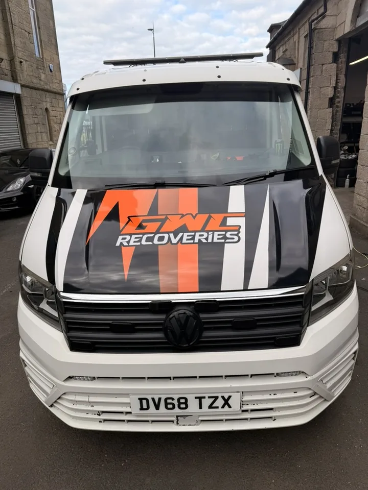 Front view of a white recovery truck with black, orange and grey bonnet graphics.