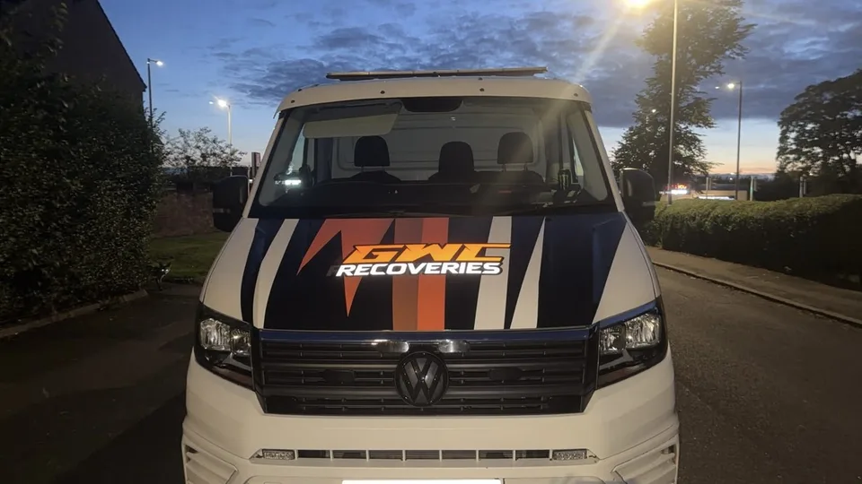 Front view of the recovery truck showing striped bonnet graphics in black, orange, grey and white.