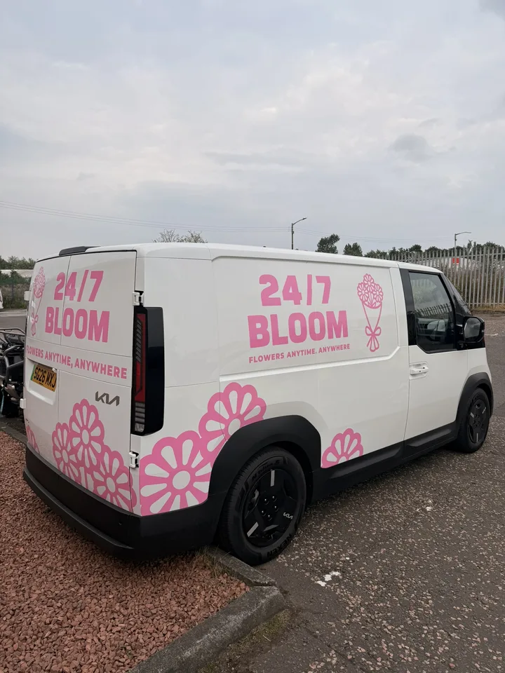 Rear three-quarter view of a white florist delivery van with bright pink lettering and flower graphics.