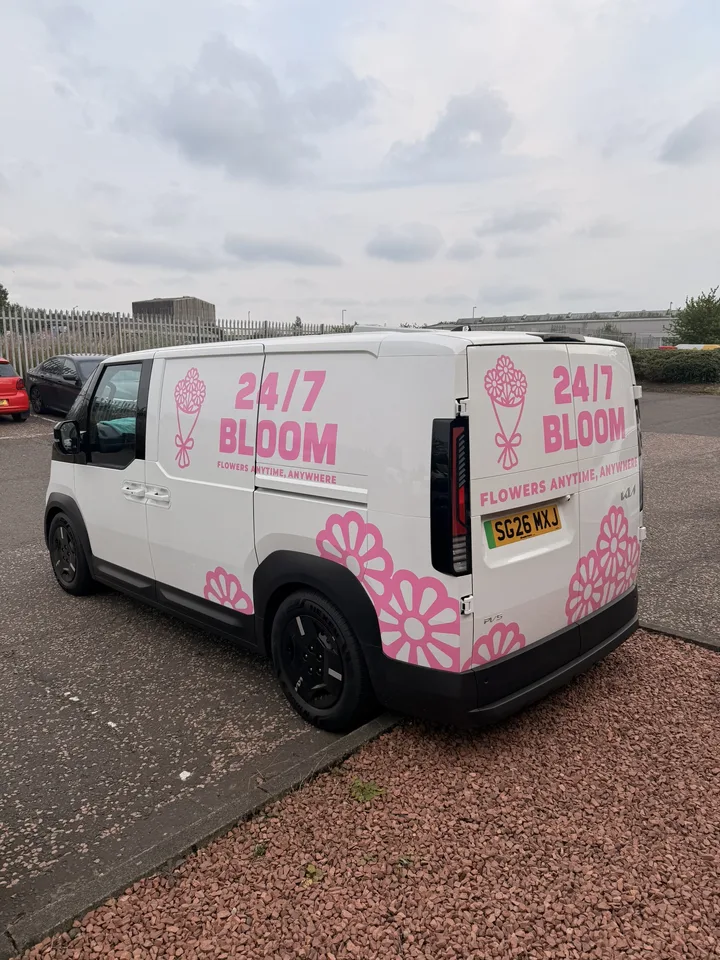 Wide rear three-quarter view of the florist van with pink graphics across the side panel and rear doors.