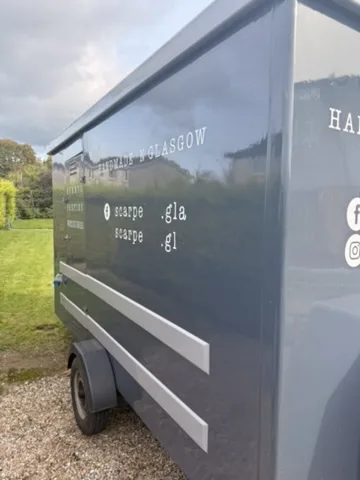 Angled side-panel view of the grey trailer with its previous lettering before the Paisley Pie Co wrap.