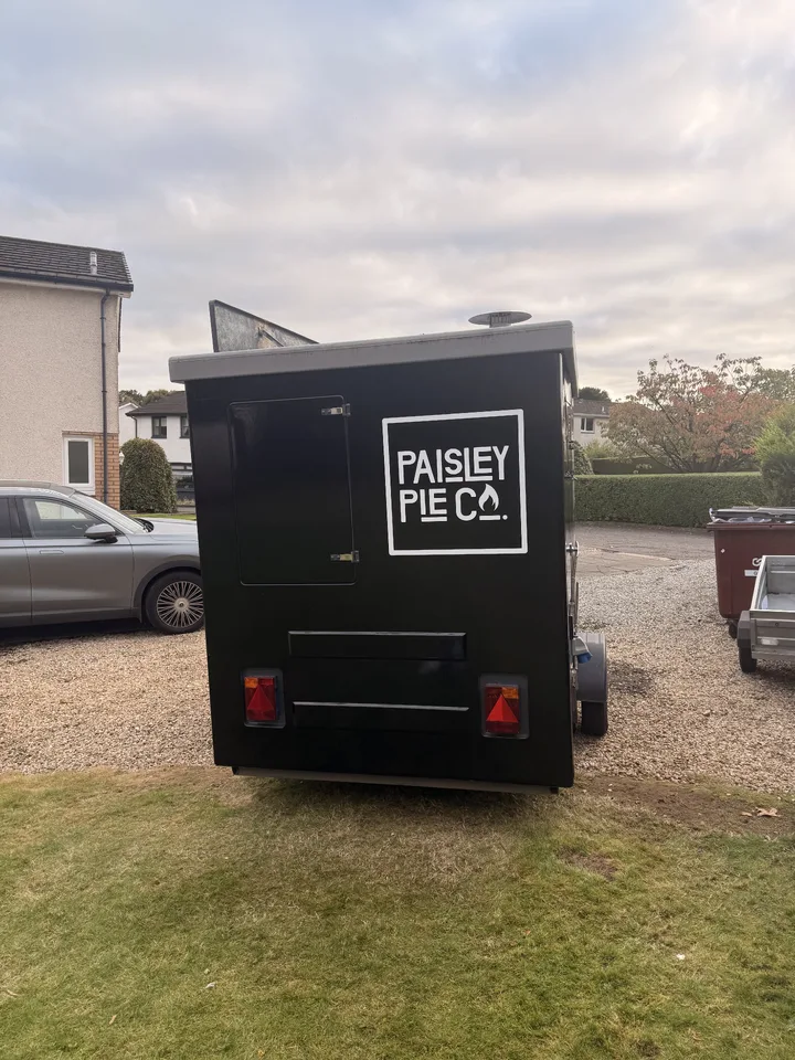 Rear of the black-wrapped Paisley Pie Co trailer with a white square logo beside the access hatch.